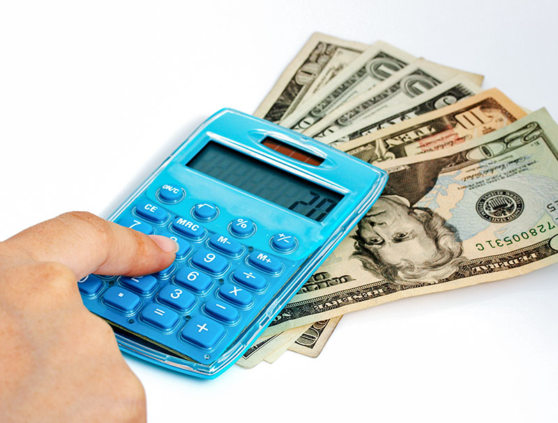 Woman's hand ready to press a button on a calculator which sits over a fanned out stack of money.