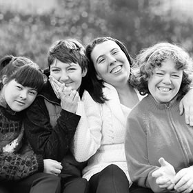 A group of four people, smiling and posing together for the camera. They are all women with disabilities. 